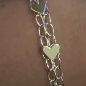 May include: A silver chain bracelet with three heart-shaped charms. The charms are silver, white, and black.