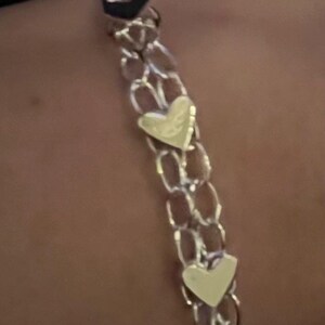 May include: A silver chain bracelet with three gold heart charms.