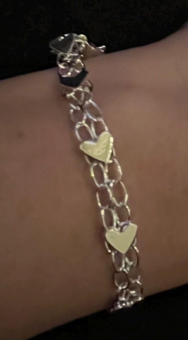 May include: A silver chain bracelet with three gold heart charms.