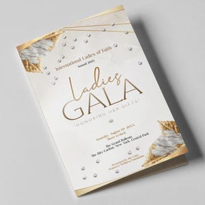 May include: A folded event program with gold accents and the text "Ladies GALA" in elegant script. The program includes the event details: "International Ladies of Faith," "Honoring Her Gifts," and the date and location. Decorative elements include gold leaf and small, sparkling embellishments.