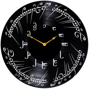 May include: A black vinyl record clock with white lettering. The lettering is in the Elvish language from the Lord of the Rings. The clock hands are gold.