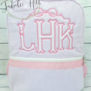 May include: A pink and white striped backpack with a pink ribbon and the monogram "LHK" embroidered on the front.