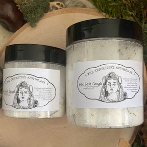 May include: Two glass jars of bath salts with black lids and white labels. The labels feature a black and white illustration of a woman with a crown and the text "The Trickster's Apothecary" and "The Last Laugh".