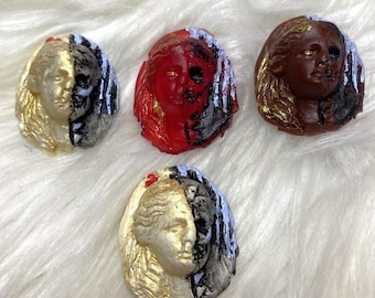 Puede incluir: Cuatro figuritas de cerámica de caras, cada una con un esquema de color diferente. Las caras están divididas en dos, con un lado dorado y el otro lado de un color diferente. Los colores son rojo, marrón, negro y dorado.