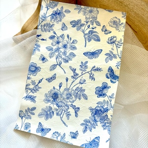 May include: A sheet of white paper with a blue floral pattern featuring butterflies and roses. The paper has a textured surface.