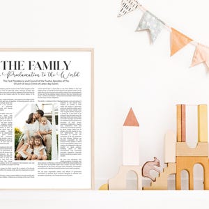 Pode incluir: Uma impress&atilde;o emoldurada com o texto "THE FAMILY A Proclamation to the World". A impress&atilde;o inclui uma foto de fam&iacute;lia e texto. A moldura &eacute; de cor clara. Blocos de madeira e uma faixa no fundo.