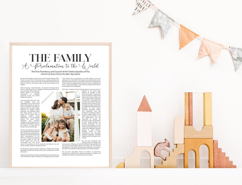 Pode incluir: Uma impress&atilde;o emoldurada com o texto "THE FAMILY A Proclamation to the World". A impress&atilde;o inclui uma foto de fam&iacute;lia e texto. A moldura &eacute; de cor clara. Blocos de madeira e uma faixa no fundo.