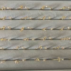 A set of 26 gold rings, each featuring a different letter of the alphabet, with a small cubic zirconoia accent. 26 letters for each available name initial - initial personalised jewellery, adjustable ring.
