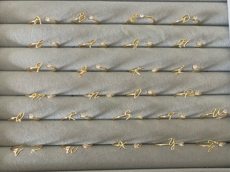 A set of 26 gold rings, each featuring a different letter of the alphabet, with a small cubic zirconoia accent. 26 letters for each available name initial - initial personalised jewellery, adjustable ring.