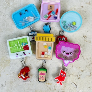 May include: A collection of medical-themed badge reels with various designs. Includes a blue container with medical tools, a purple jar with biohazard symbols, and a clear reel with floating elements. Other reels feature a heart, pills, and a brain.
