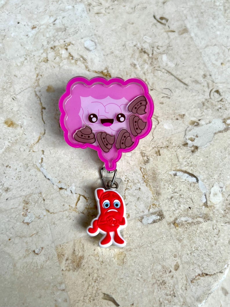 May include: A pink and light purple badge reel featuring a cartoon illustration of intestines with smiling faces and brown poop emojis. A red, sad-faced stomach charm hangs below.