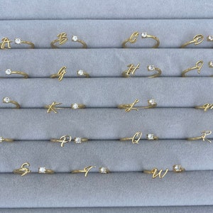 A set of 26 gold rings, each with a single clear stone and a cursive letter from A to Z. Personalised adjustable rings, gold jewellery, CZ jewellery, gift.