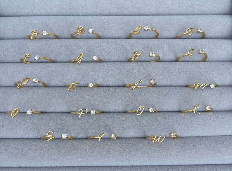 A set of 26 gold rings, each with a single clear stone and a cursive letter from A to Z. Personalised adjustable rings, gold jewellery, CZ jewellery, gift.
