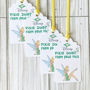 May include: Four white gift tags with scalloped edges and yellow ribbons. Each tag features the Disney logo, a cartoon image of Tinkerbell, and the text "PIXIE DUST FROM YOUR PALS" in green. The tags are hanging against a light wood background.