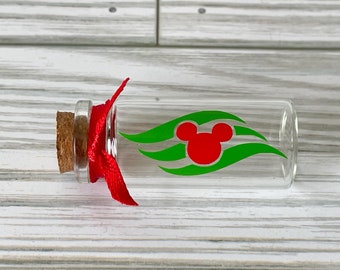 May include: A clear glass bottle with a cork stopper and a red ribbon tied around the neck. The bottle features a red Mickey Mouse head logo with green wave accents. The bottle is on a white wooden surface.