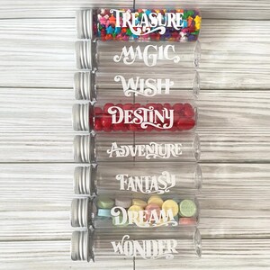 May include: Clear glass tubes with silver lids, filled with colorful candies. Each tube is labeled with a white script word: Treasure, Magic, Wish, Destiny, Adventure, Fantasy, Dream, and Wonder. The tubes are arranged vertically.