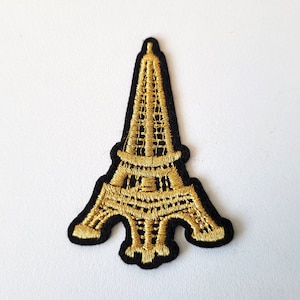 May include: Gold embroidered iron-on patch of the Eiffel Tower on a black background.