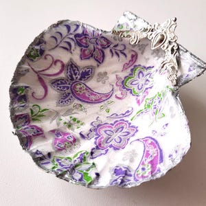 Peut inclure: Un plat décoratif en forme de coquille avec un fond blanc et un motif floral violet et vert. La coquille a un accent en métal argenté sur le dessus.