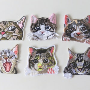 May include: Six embroidered iron-on patches featuring different cat faces. The cats are all brown, white, and gray with pink noses and whiskers. The patches are perfect for adding a touch of whimsy to clothing, bags, or other fabric items.