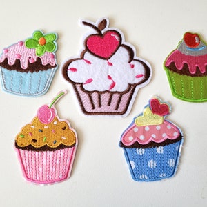 Op de afbeelding: Vijf geborduurde strijkbare cupcake-patches in verschillende kleuren en ontwerpen. De patches zijn roze, blauw, groen, bruin en geel.