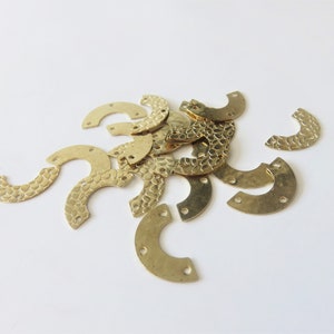 Op de afbeelding: Een stapel gouden metalen halve cirkels met een getextureerd oppervlak en drie gaten.