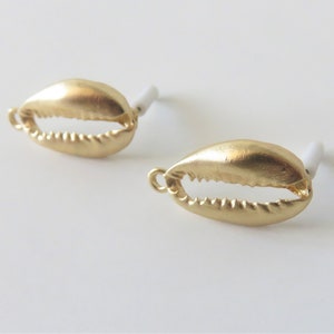 Può includere: Un paio di orecchini a forma di conchiglia color oro. Gli orecchini sono piccoli e delicati, e hanno un design semplice ed elegante.