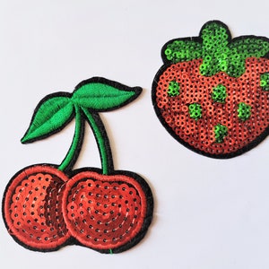 Peut inclure: Deux patchs thermocollants en sequins rouges et verts, l'un représentant une cerise et l'autre une fraise.