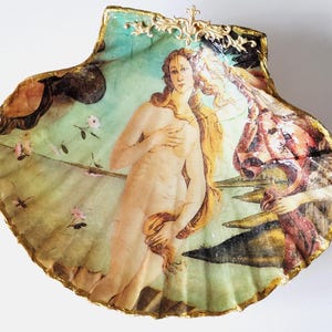 Può includere: Una conchiglia con un bordo dorato, decorata con un dipinto della Nascita di Venere, una famosa opera del Rinascimento. Il dipinto raffigura una donna nuda in piedi su una conchiglia, con una figura di un dio sullo sfondo.