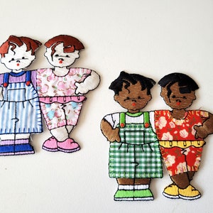 Op de afbeelding: Geborduurde patches met twee paar gestileerde figuren. Eén paar draagt blauw-wit gestreepte overalls en outfits met bloemenprint. Het andere paar draagt groen geruite en rood bloemen outfits. Elke patch heeft bruin haar en is zwart omlijnd.
