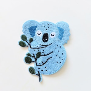 May include: A blue embroidered koala bear patch with green leaves. The koala is holding a branch with leaves.