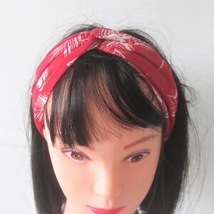Peut inclure: Un bandeau rouge avec un motif floral blanc. Le bandeau est torsadé et noué en haut.