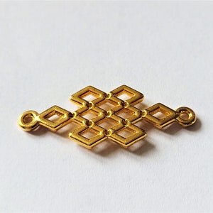 以下が含まれることがあります： 結び目を模した幾何学模様の金色の金属製チャーム。チャームの両側に小さなループが2つあります。