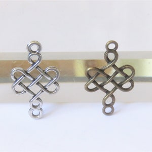 May include: Two silver and bronze metal charms in the shape of a Celtic knot. The charms are about 2 inches long and have a loop at the top for attaching to a necklace or bracelet.