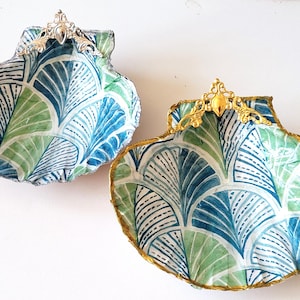 Può includere: Due piatti decorativi a forma di conchiglia con un motivo geometrico blu e verde. Ogni piatto ha un manico in metallo dorato.