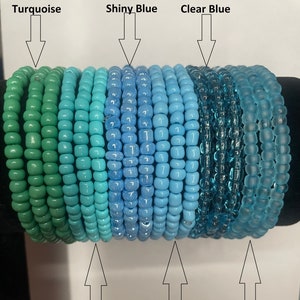 May include: A collection of colorful beaded bracelets in shades of turquoise, blue, and green. The bracelets are arranged in a gradient from turquoise to green, with shades of blue in between. The bracelets are made of small, round beads.