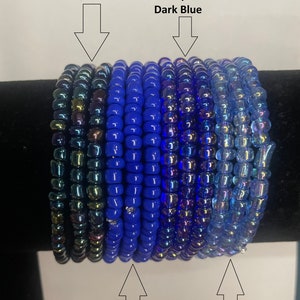May include: A stack of blue and iridescent glass beads in various shades of blue, including chrome blue, dark blue, transparent dark blue, and transparent royal blue.