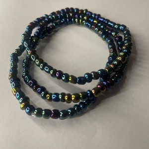 K&ouml;nnte beinhalten: Eine mehrreihige Perlenkette mit schillernden blauen, gr&uuml;nen und goldenen Perlen.