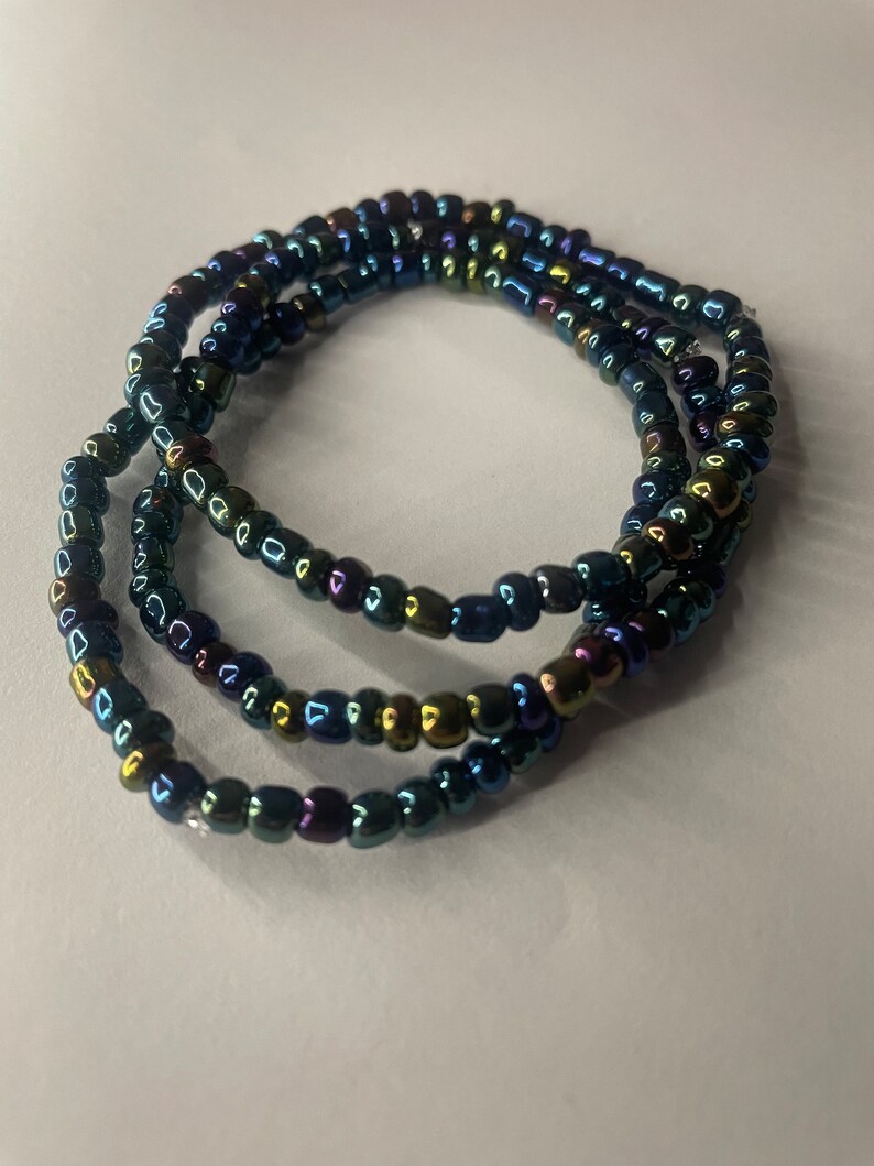 K&ouml;nnte beinhalten: Eine mehrreihige Perlenkette mit schillernden blauen, gr&uuml;nen und goldenen Perlen.
