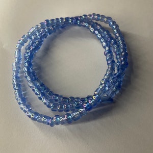 K&ouml;nnte beinhalten: Eine blaue Perlenkette mit schillernden Perlen. Die Kette ist zu einem Kreis gewickelt.