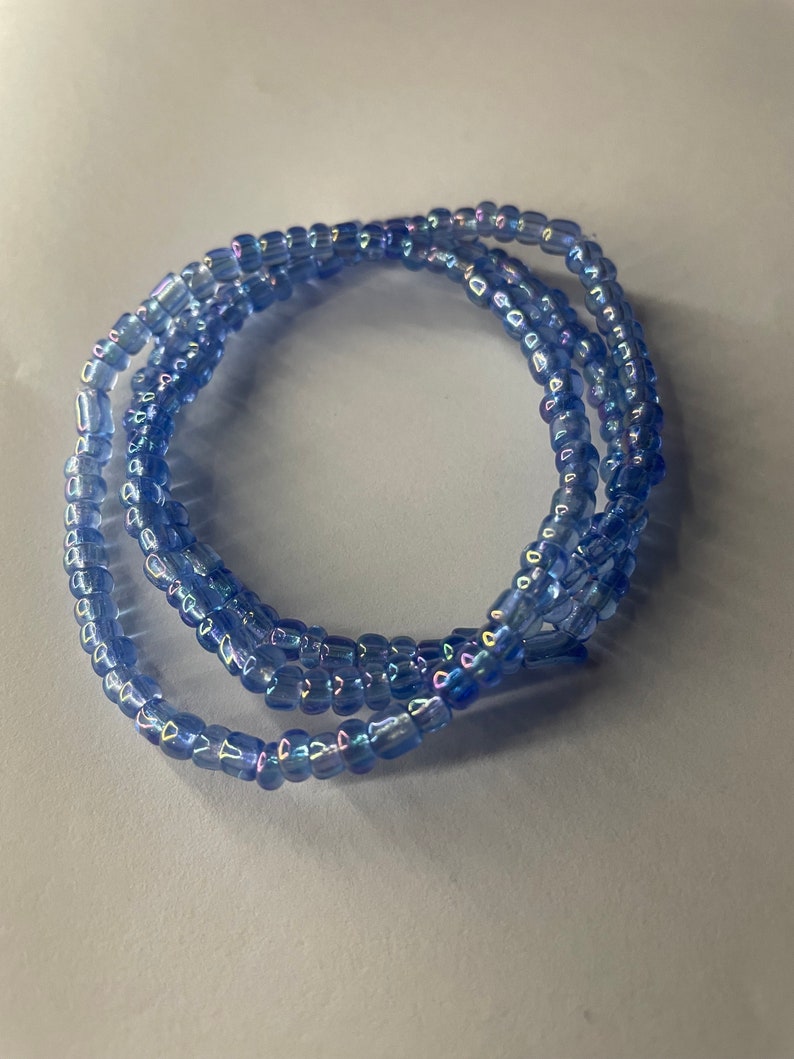 K&ouml;nnte beinhalten: Eine blaue Perlenkette mit schillernden Perlen. Die Kette ist zu einem Kreis gewickelt.