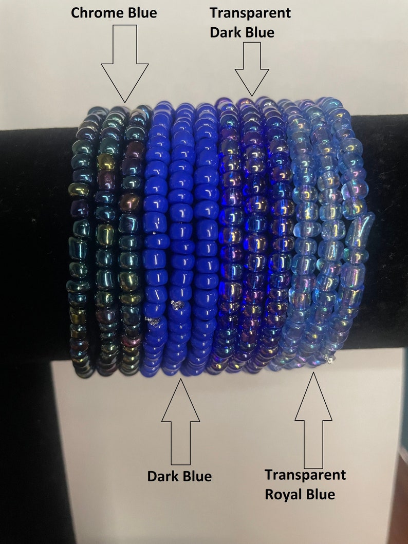 K&ouml;nnte beinhalten: Ein Stapel blauer und irisierender Glasperlen in verschiedenen Blaut&ouml;nen, darunter Chromblau, Dunkelblau, transparentes Dunkelblau und transparentes K&ouml;nigsblau.