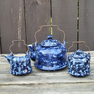 May include: Three blue and white ceramic teapots with a speckled design. The largest teapot has a handle and spout, while the two smaller teapots have handles but no spouts.