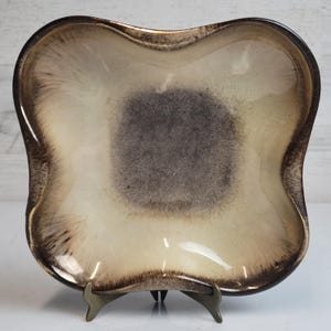 May include: A square-shaped ceramic serving dish with a wavy edge. The dish has a brown and white glaze with a mottled effect.
