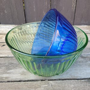 Może przedstawiać: Dwie szklane miski, jedna zielona, a druga niebieska, z żebrowanym wzorem. Miski są włożone jedna w drugą.