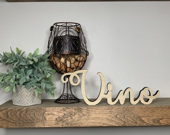 May include: A wooden shelf with a decorative wine cork holder, a small potted plant, and a wooden sign that says "Vino".