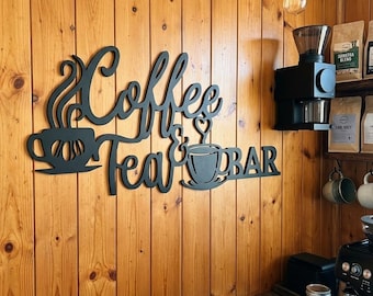 May include: A black metal wall sign featuring the words Coffee & Tea BAR in a cursive script font. The sign includes two cup icons, one with steam rising and one with a heart-shaped steam design, mounted on a vertical wood panelled wall.