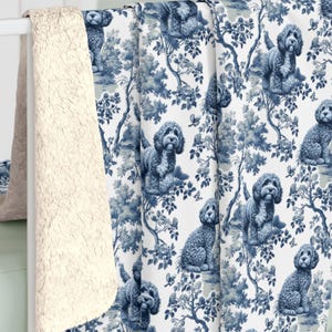 May include: A blue and white patterned blanket featuring a toile design with dogs and trees. The blanket has a soft, cream-colored sherpa lining. The blanket is draped over a white crib.