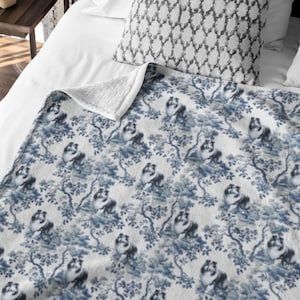 May include: A white fleece throw blanket with a blue and white pattern of dogs in a floral setting.