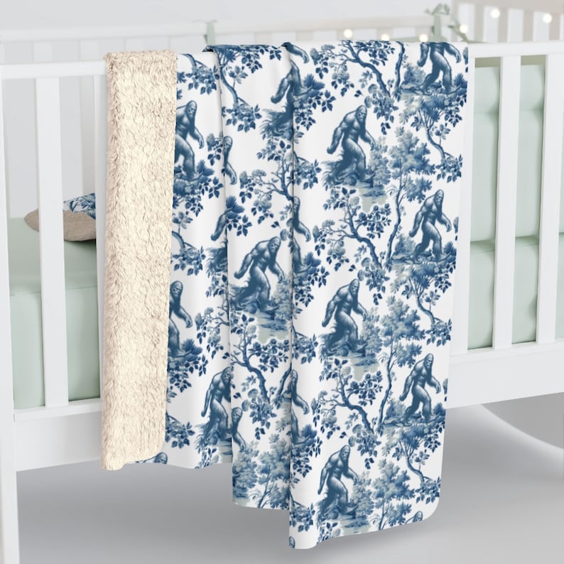 May include: A white and blue throw blanket featuring a repeating pattern of a Bigfoot walking through a forest. The blanket has a soft, plush feel and is ideal for adding a touch of whimsy to any room.