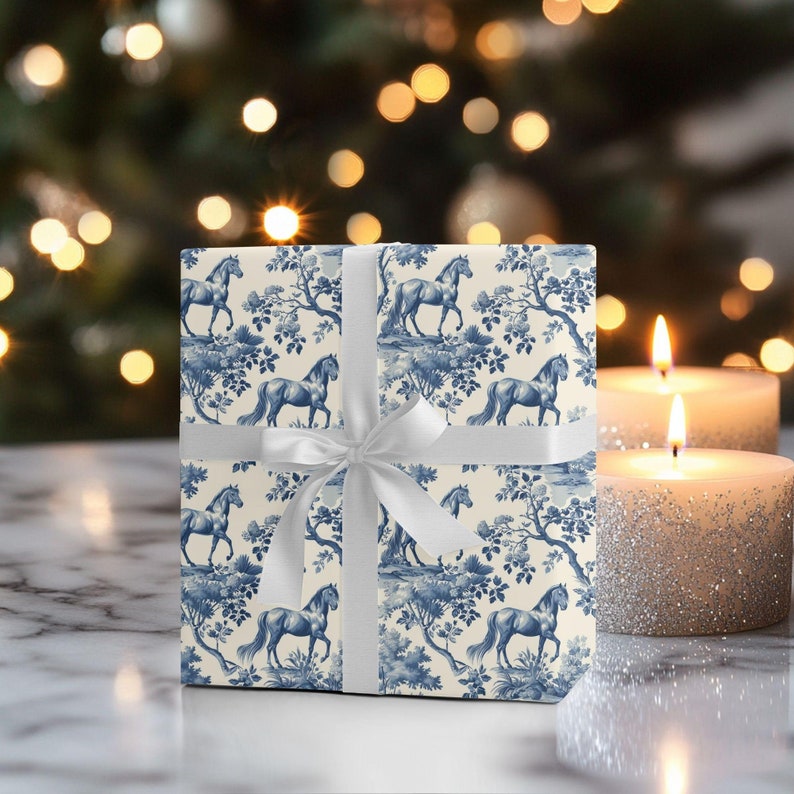 May include: A white gift box with a blue and white horse pattern. The box is tied with a white ribbon and is sitting on a white surface.